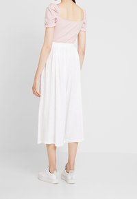 Ljusrosa ribbad topp med puffärmar och fyrkantig halsringning, kombinerad med en knälång vit linneskirt och vita sneakers.