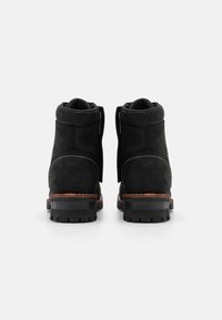 Botas de tobillo de ante negro con un acabado texturizado, que presentan una cremallera lateral, suela de goma y un detalle de madera en el tacón.
