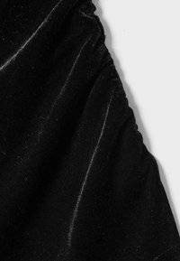 Tessuto in velluto nero con bordo elastico arricciato che crea morbide pieghe su uno sfondo chiaro.