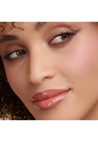 Nærbilde av et ansikt med krøllete hår. Kjennetegn inkluderer lys brun hud, glansfulle lepper, myk rosa rouge, og nøytral øyeskygge med definerte vipper.