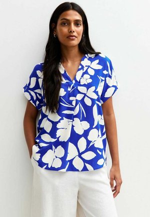 Blouse bleue à manches courtes avec un col en V, présentant de grands motifs floraux blancs et une coupe décontractée. Le matériau semble léger et lisse.