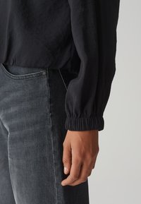 Zwarte lange mouwen shirt met geplooide manchetten, gecombineerd met donkergrijze denim jeans. Soepele stofstructuur, slim fit en minimalistische stiksels.