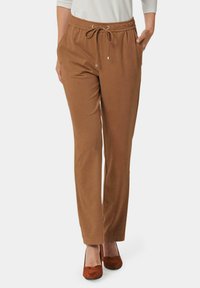 Pantalons marron à taille élastique avec cordon de serrage, en tissu doux, jambes fuselées et poches latérales, associés à des talons fermés marron.