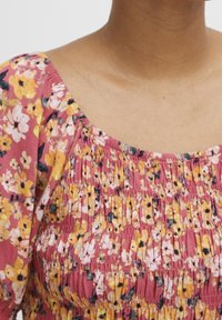 Kwiatowa sukienka z różowym tłem, z żółtymi i białymi kwiatami. Żabotowa struktura przy dekolcie i rękawach, tworząca marszczenie.