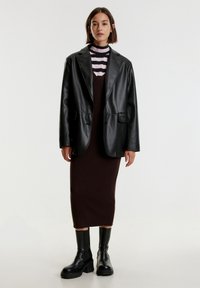 Zwarte leren blazer over een bruine geribde jurk, gelaagd met een roze en zwart gestreepte coltrui. Zwarte enkellaarsjes met dikke zolen.