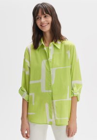 Green patterned button-up shirt with rolled sleeves, featuring abstract white geometric shapes, lightweight fabric, and a classic collar.