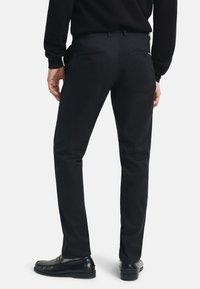 Pantalones negros de corte slim, material de mezcla de algodón, con bolsillos traseros con botones y una superficie suave y texturizada.