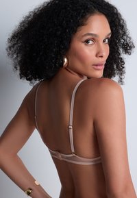 Soutien-gorge nu avec fines bretelles, présentant un matériel réglable. Texture de tissu lisse avec un design minimaliste. Accents dorés sur les bretelles.