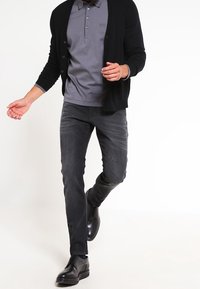 Tmavě šedé džíny, šedé polo tričko a černý kardigan přes to. Černé kožené boty dodávají elegantní vzhled. Jednoduchý design s knoflíkovými detaily.