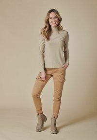 Beige metallischer Oberteil mit langen Ärmeln, kombiniert mit beigen Cargo-Hosen mit Seitentaschen und beigefarbenen Stiefeln in Knöchelhöhe mit strukturierten Sohlen.