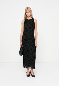 Zwarte jurk met bloemenprint, sleeveless ontwerp, gladde textuur en een vloerlange snit. Gecombineerd met een zwarte handtas en hakken.