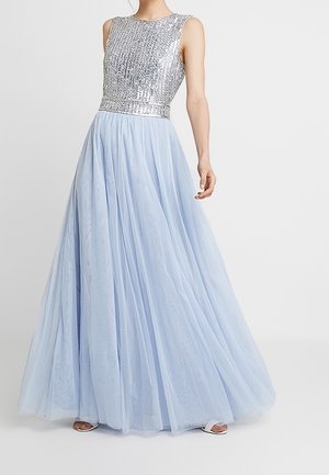 Ärmelloses Abendkleid mit silbernem Pailletten-Oberteil und fließendem hellblauem Tüllrock, getragen mit offenen Schuhen.