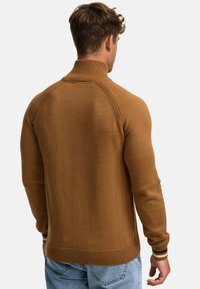 Bruine gebreide trui met een hoge kraag, geribde manchetten en zoom. Heeft een gestructureerd patroon met een slim-fit ontwerp. G gedragen met lichtblauwe jeans.
