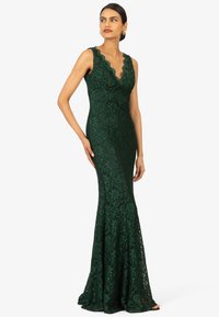 Grünes Spitzenkleid mit Blumenmuster, gewelltem Ausschnitt, ärmellosem Design, taillierter Oberteil und ausgestellt geschnittenem Rock.