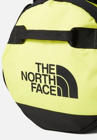 Dzeltena un melna sporta soma ar "THE NORTH FACE" zīmolu, izgatavota no izturīga materiāla ar strukturētu formu un augšējiem nesamajiem siksnām.