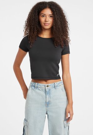 Tricou negru scurt cu mâneci scurte, realizat dintr-un material neted. Are un gât rotund și un mic logo pe față. Este purtat cu blugi lejeri de culoare albastru deschis.