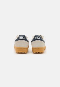 Nike sporta apavi ar beiga zamšas augšdaļu, tumši zila akcenti un gumijas zole. Izceļas ar drosmīgu 'NIKE' logo uz papēža.