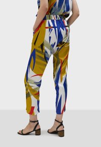 Pantaloni a fantasia multicolore con una vestibilità comoda, che presentano tonalità di giallo, blu, rosso e verde. Inclusi tasche e cintura elastica.