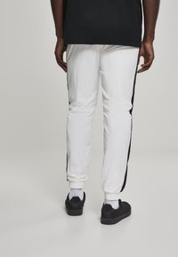 Hvite idretts joggebukser med svarte side stripe, lettvektsstoff, elastiske mansjetter, kombinert med svarte joggesko og hvite ankelstrømper.