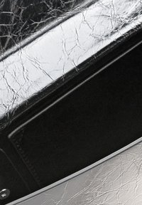 Interno di una borsa in pelle nera con una texture lucida, dettagli in argento e un design con bordi lisci e curvi, con un'area tasca visibile.