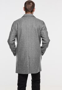 Grå ullkappa med notched krage, enkel bakventil och skräddarsydd silhuett, styltad med något överdimensionerade ärmar.