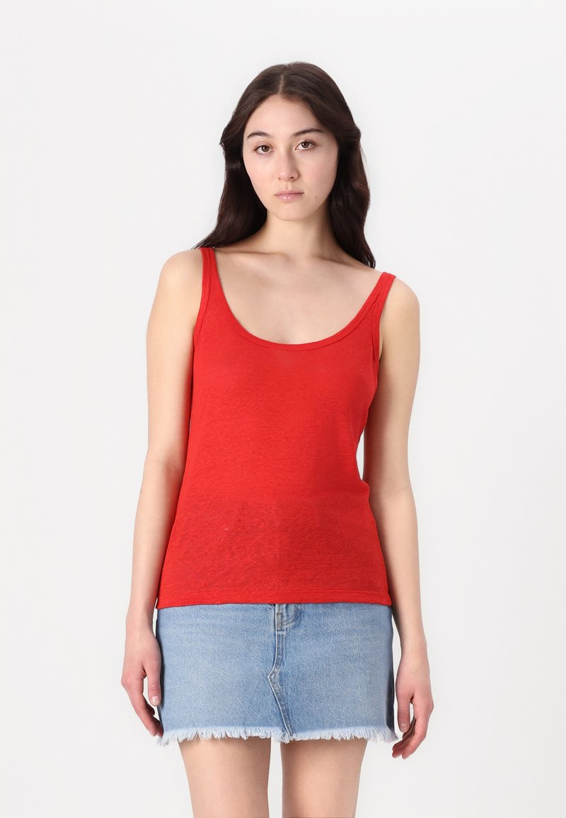 Débardeur en coton rouge avec un décolleté arrondi et de larges bretelles, associé à une jupe en denim bleu clair avec un ourlet effiloché.
