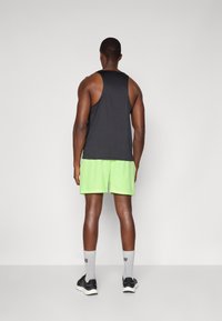 Schwarzes ärmelloses Tanktop, leuchtend grüne Shorts, graue Socken und schwarze Turnschuhe. Glatte Stoffqualität, lockere Passform und kontrastierende Farben.
