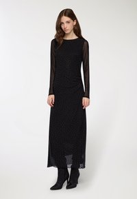 Czarna sukienka z długim rękawem, dopasowaną górą i zwiewnym dołem, z małymi srebrnymi kropkami, warstwowym przezroczystym materiałem i czarnymi botkami sięgającymi kostki.