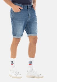 Shorts en denim bleu clair, avec des ourlets retroussés, un design classique à cinq poches et une fermeture éclair, associés à des chaussettes blanches et des baskets.