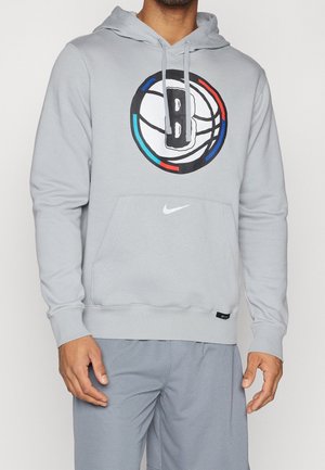 Man wearing light gray hoodie with Brooklyn Nets basketball logo and white Nike swoosh, paired with matching gray shorts.