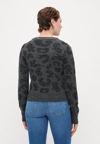 Maglione grigio con stampa leopardata nera, impreziosito da sottili luccichii. Presenta un collo rotondo e orli e polsini a coste.
