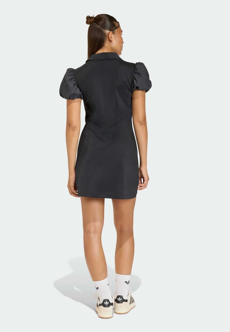 Abito nero con maniche a sbuffo e design aderente. Abbinato a calzini bianchi e scarpe da ginnastica nere, che mettono in risalto le texture e gli accenti minimalisti.