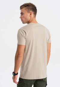 Béžové tričko s krátkým rukávem vyrobené z měkké bavlny, s kulatým výstřihem a volným střihem, s hladkou texturovanou tkaninou a rovním lemem.