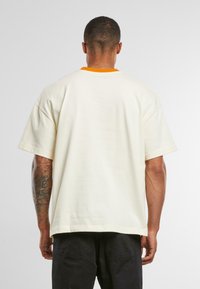 T-shirt crème à manches courtes avec un col orange vif. Texture douce et coupe décontractée, vue de dos, montrant un design simple.