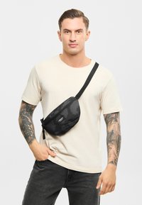 Čierna textúrovaná taška cez telo so zipsom, s malou nášivkou loga. S nastaviteľným popruhom a zakriveným tvarom.