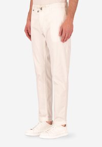 Pantaloni in cotone bianchi con una vestibilità rilassata, dotati di vita con cordoncino e caviglie affusolate, abbinati a sneakers bianche.