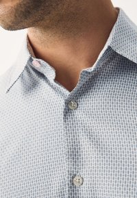 Világoskék ing texturált mintával, terített gallérral és két gombbal, enyhén geometriai mintázattal.