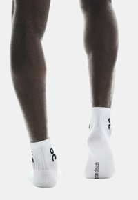 Calcetines de tobillo blancos con textura acanalada y logotipo negro en los lados exteriores. Diseño de punta sin costuras, que muestra una suave construcción de algodón.
