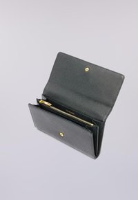 Černá texturová kožená peněženka otevřená, ukazující zlatý zipový prostor a uzávěr na patentku na světle šedém pozadí.