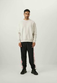 Sweatshirt gris clair, pantalon noir avec des rayures latérales pink et blanches, et baskets noires. Tissu lisse, coupe décontractée, design simple.