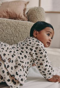 Leopard-patterned romper in soft fleece, featuring black and tan spots on a cream background. Long sleeves with a rounded hem.