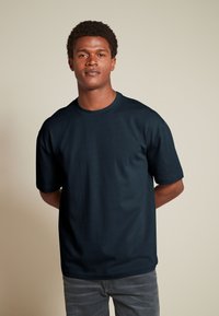 Mørkeblå t-shirt med korte ærmer, rund halsudskæring, glat tekstur og en afslappet pasform. Bæres med grå tætsiddende jeans.