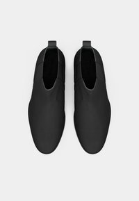 Zapatos negros tipo slip-on hechos de material suave, con un diseño minimalista, punta redondeada y acentos elásticos para facilitar el uso.