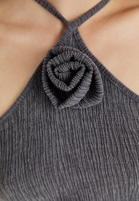 Γκρι φόρεμα με υφή και πτυχώσεις, που αναδεικνύεται από μια γκρι ροζέτα από ύφασμα στη λαιμόκοψη.