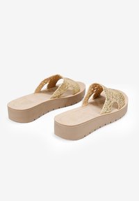 Sandales à glissière en paille tressée avec une plateforme en caoutchouc beige, présentant des lanières croisées et une semelle intérieure texturée pour une adhérence et un confort optimal.