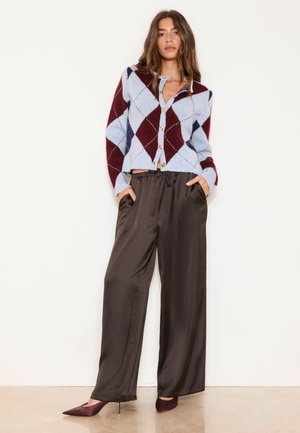 Naine, kes kannab sinise ja burgundiaatoonilise nuppudega argyle-kardigaani, seda on kombineeritud lahtiste mustade satiinpükstega ja burgundiatooniliste teravate kontsadega.