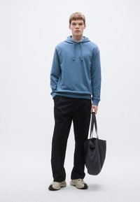 Sweatshirt azul em algodão com cordões, calças largas pretas e uma bolsa tote escura, usados com ténis creme e pretos. Design simples e minimalista.