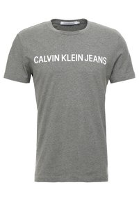 Camiseta de algodón gris con cuello redondo y mangas cortas, con "CALVIN KLEIN JEANS" impreso en relieve en letras blancas en la parte frontal.