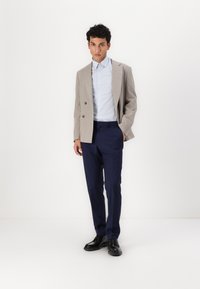Világosszürke, texturált blazer két gombbal, világoskék csíkos inggel és sötétkék nadrággal párosítva. Fekete fűzős cipővel kiegészítve.