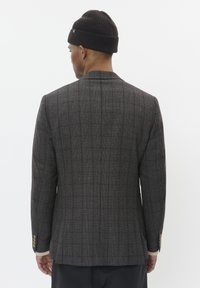Blazer de cuadros grises con solapas y textura en la tela, y detalles de botones dorados en las mangas. Combinado con un gorro de punto oscuro.
